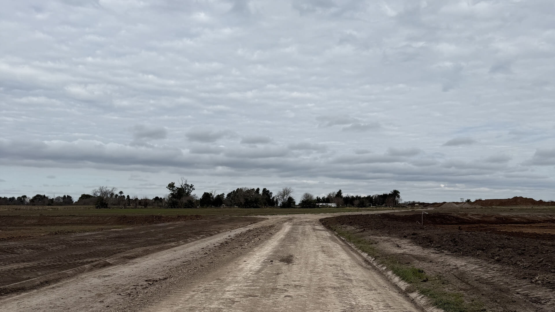 Camino de tierra dentro de un nuevo loteo en desarrollo bajo un cielo nublado