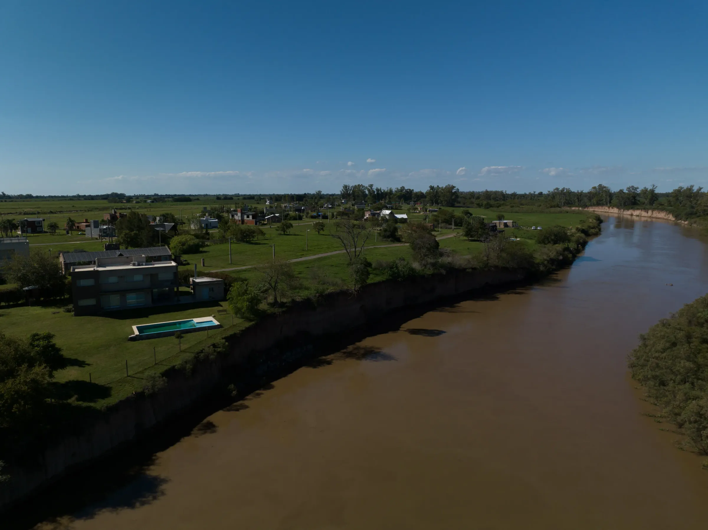 Vista aérea de un pueblo a orillas del río rodeado de campos verdes y casas modernas
